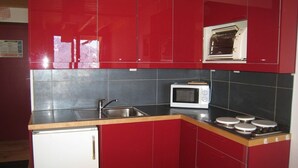 A compact kitchen with red cabinets, a white microwave, a sink, and a small refrigerator. - Cozy Duplex for 5, Close to Ski Lifts & Shops, South-Facing Balcony – Alpe d'Huez (Huez)