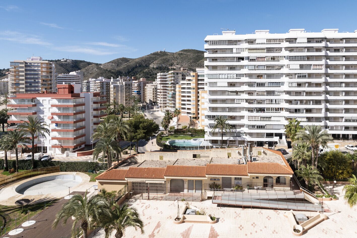 A coastal hotel with multiple floors, a swimming pool, and palm trees.