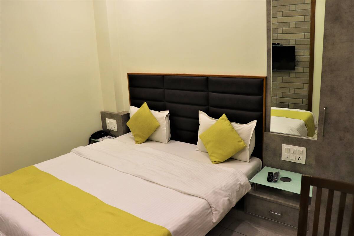 A neatly made bed with a headboard, a bedside table with a remote control, and a wall-mounted TV.