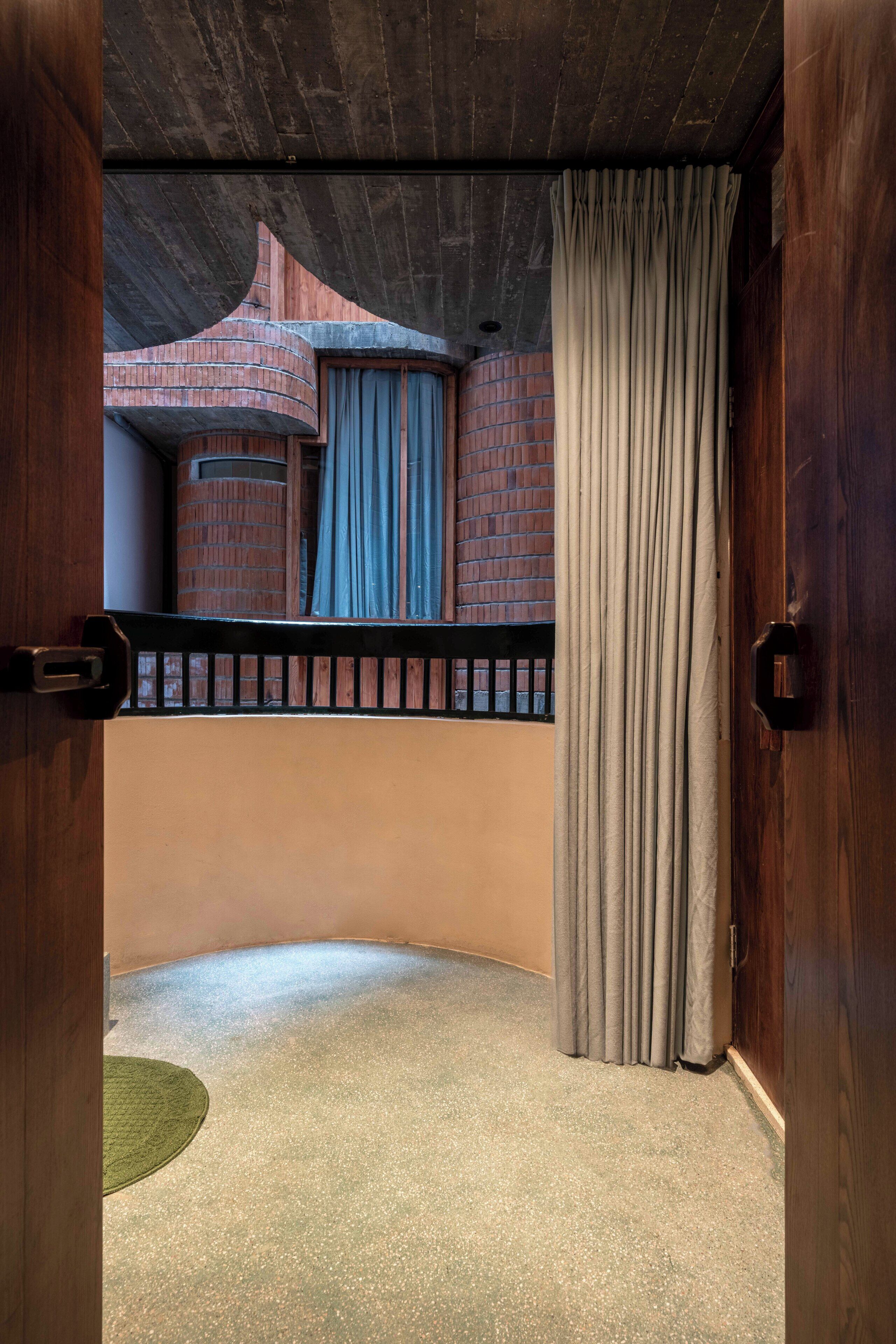 A room with a curved ceiling, a balcony with a black railing, and a view of a brick building.