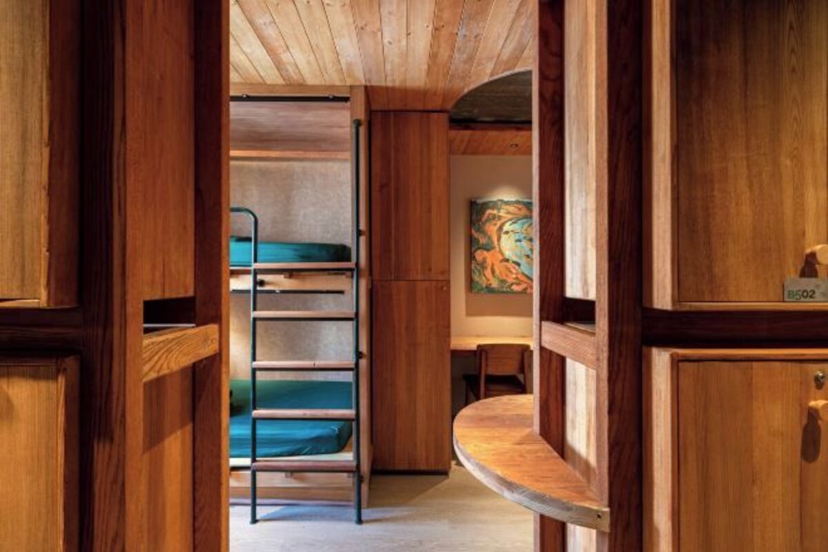 Een houten interieur met een stapelbed, een bureau en een schilderij aan de muur.