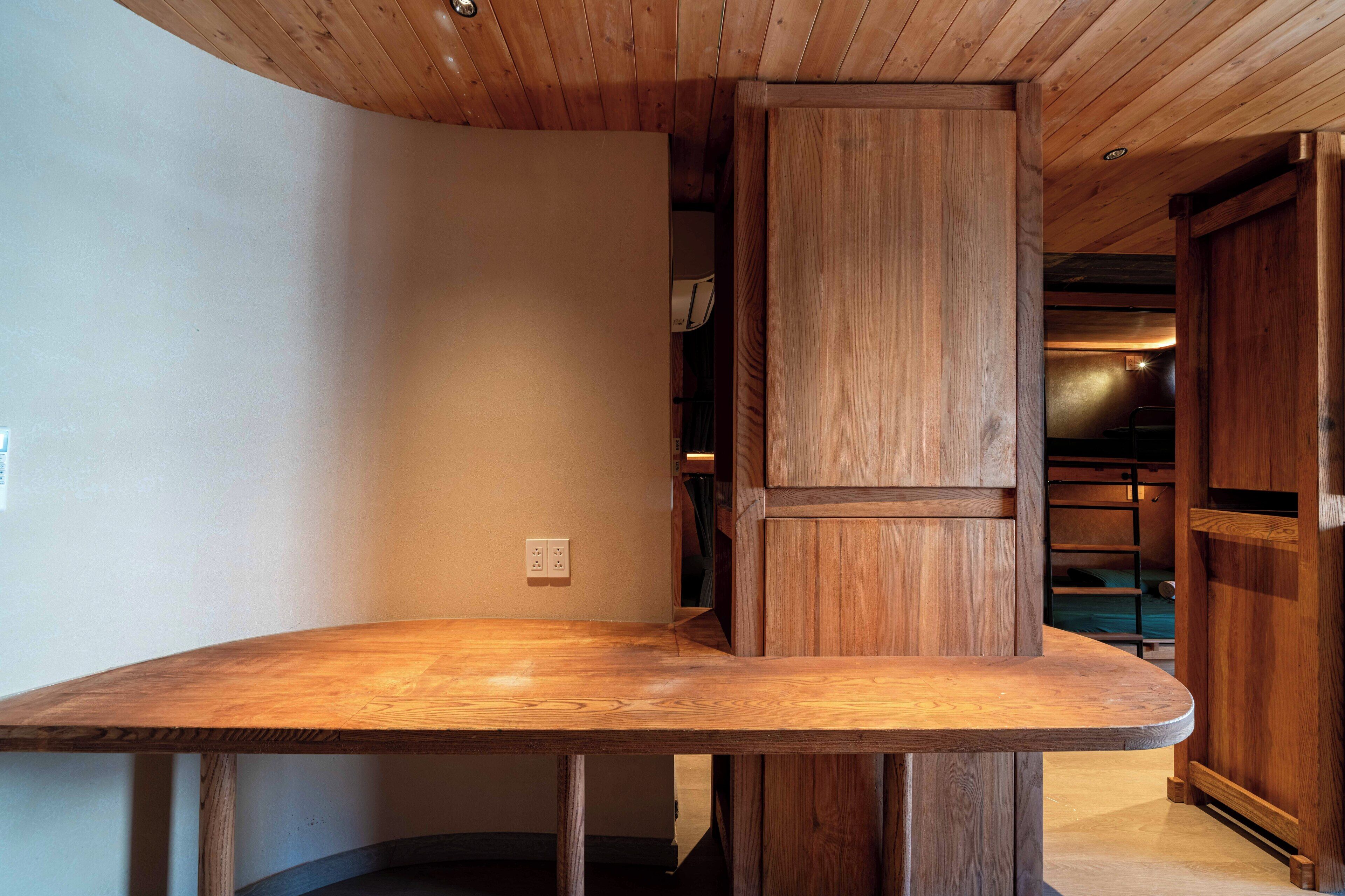 A wooden dining table with a curved edge, positioned under a wooden ceiling with a recessed light fixture.