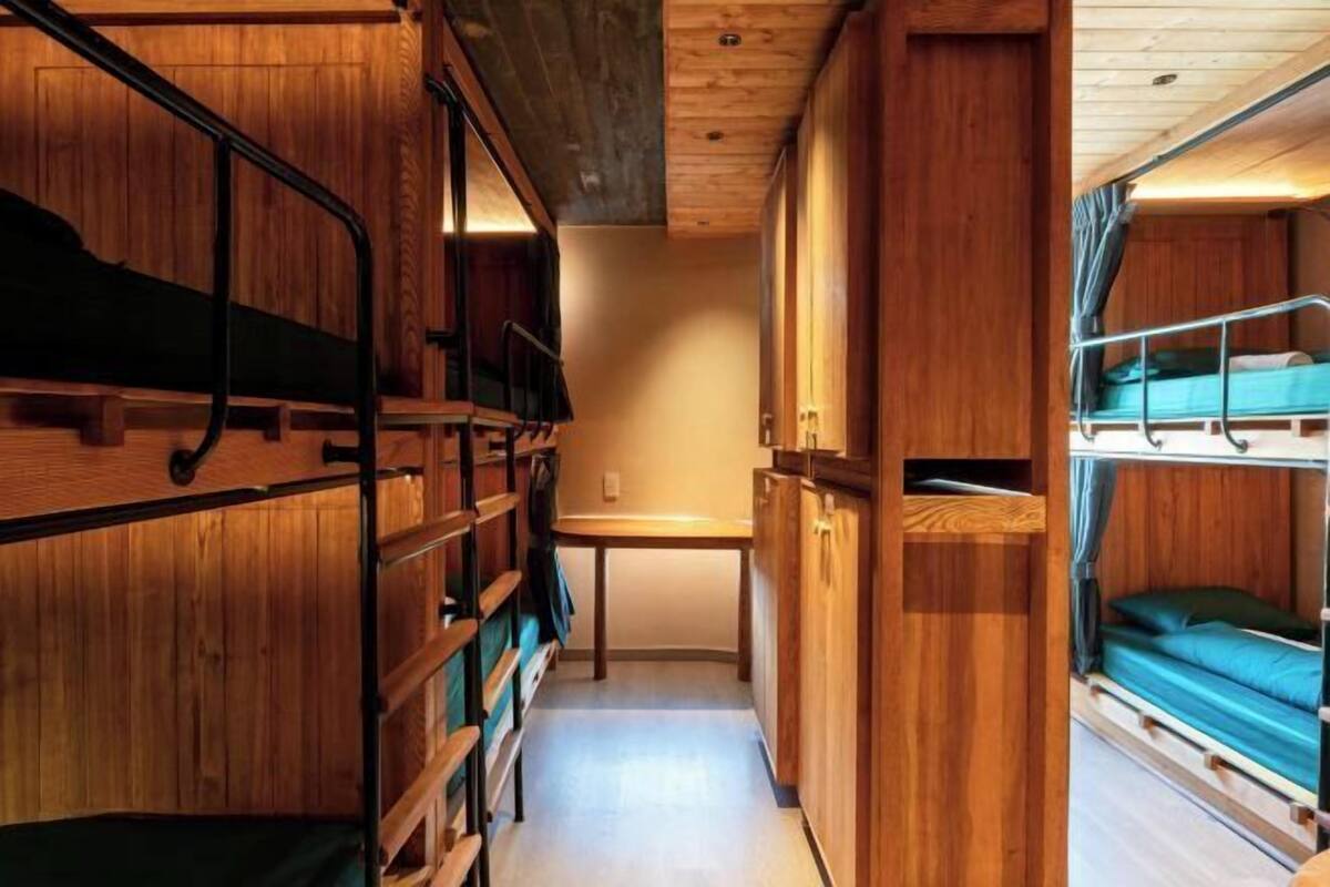 A narrow corridor with bunk beds on either side, wooden walls, and a small table in the center.
