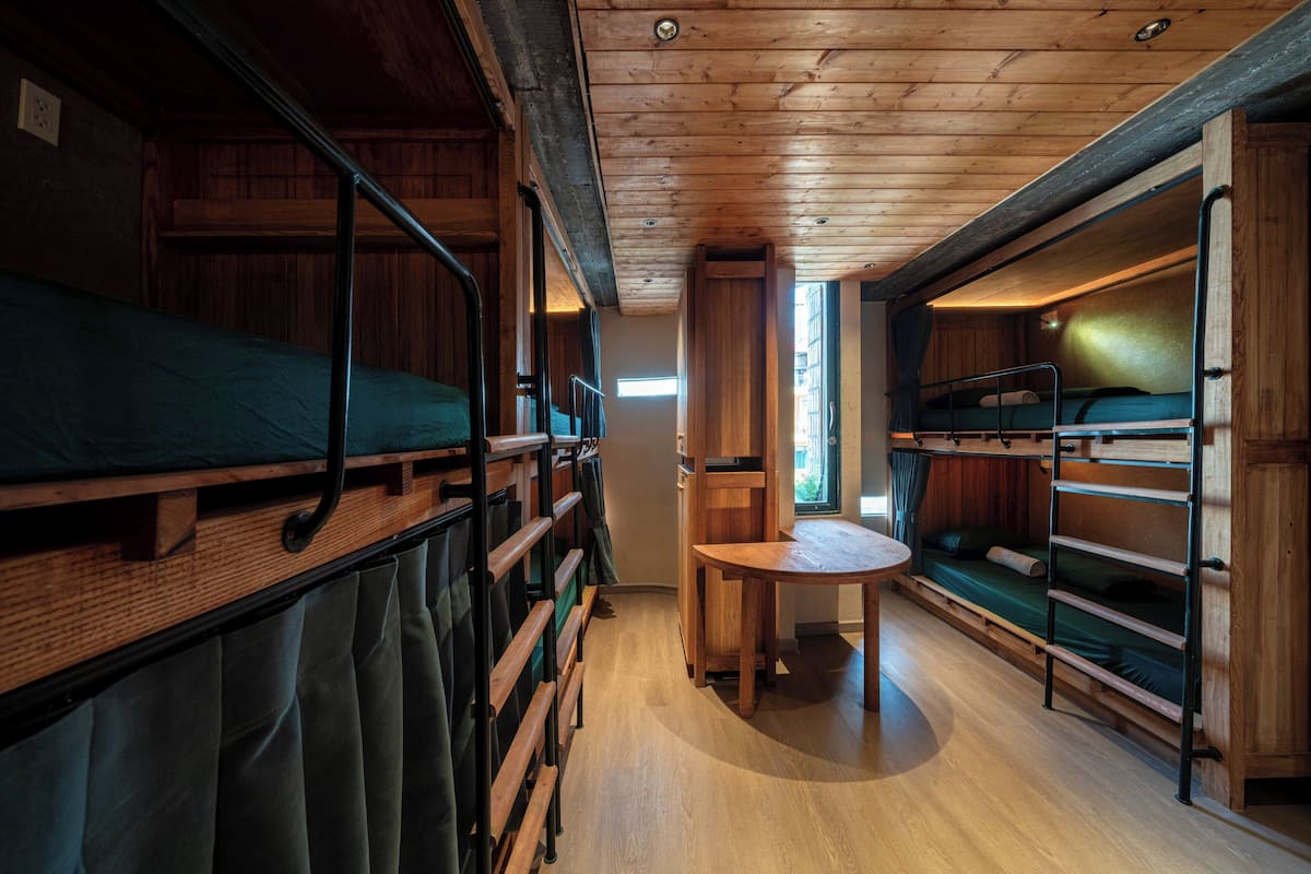 A cabin interior with bunk beds, a small table, and a window providing natural light.