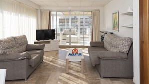 A modern living room with two grey sofas, a flat-screen TV, and a coffee table with a logo. - LIDER, 12-A (Cullera)