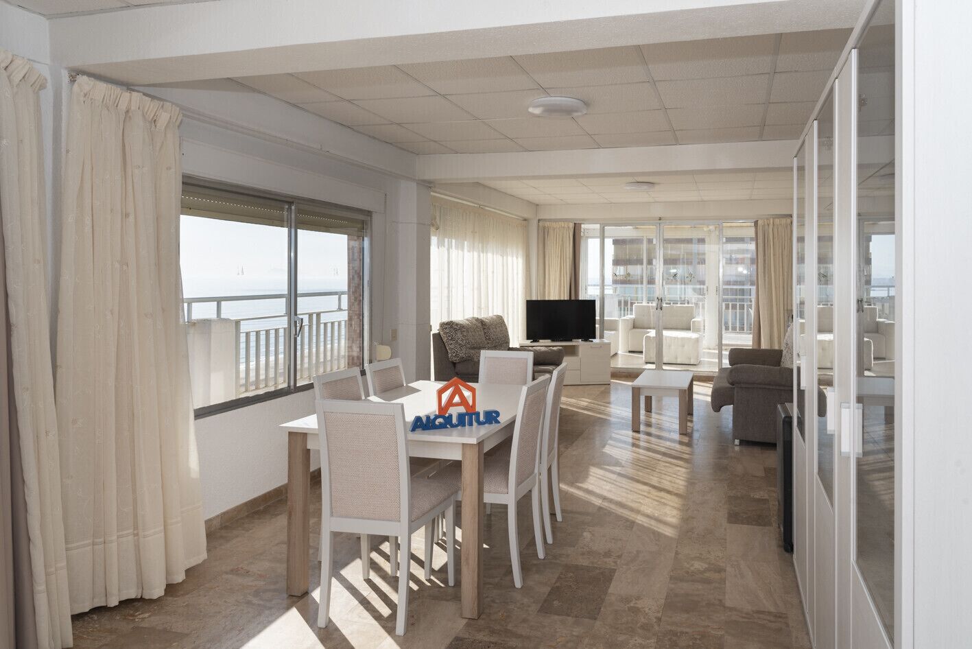 A spacious living area with a balcony, a dining table, and a TV.