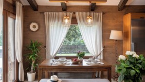 A dining area with a wooden table set for two, a potted plant, and a window with curtains. - Rural house surrounded by mountains with swimming pool, skatepark and children's playground in Llerena (Ribera de los Molinos, Llerena)