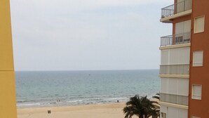 A view of a beach from a balcony with a building on one side and a palm tree-lined walkway leading to the beach. - PROVENCE, 5º-18 (Cullera)