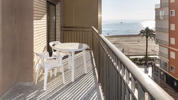 A balcony with a table and chairs, overlooking a beach and ocean. - PROVENCE, 5º-18 (Cullera)