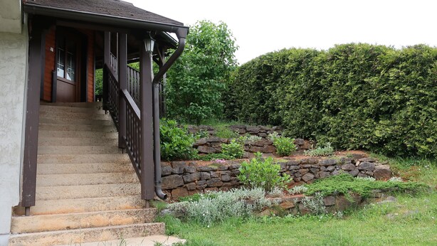 A wooden staircase leading to a covered porch with a stone retaining wall and a hedge in the background. - Apartment Jan, Pakaljski odvojak 4, 53220 Otočac, Licko-Senjska county, Croatia (Otočac)