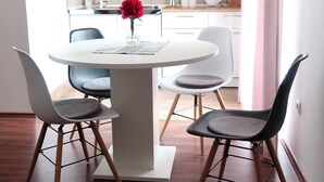 A dining area with a white table and chairs, a vase with a red flower, and a view of a kitchen and dining area in the background. - Apartment Jan, Pakaljski odvojak 4, 53220 Otočac, Licko-Senjska county, Croatia (Otočac)