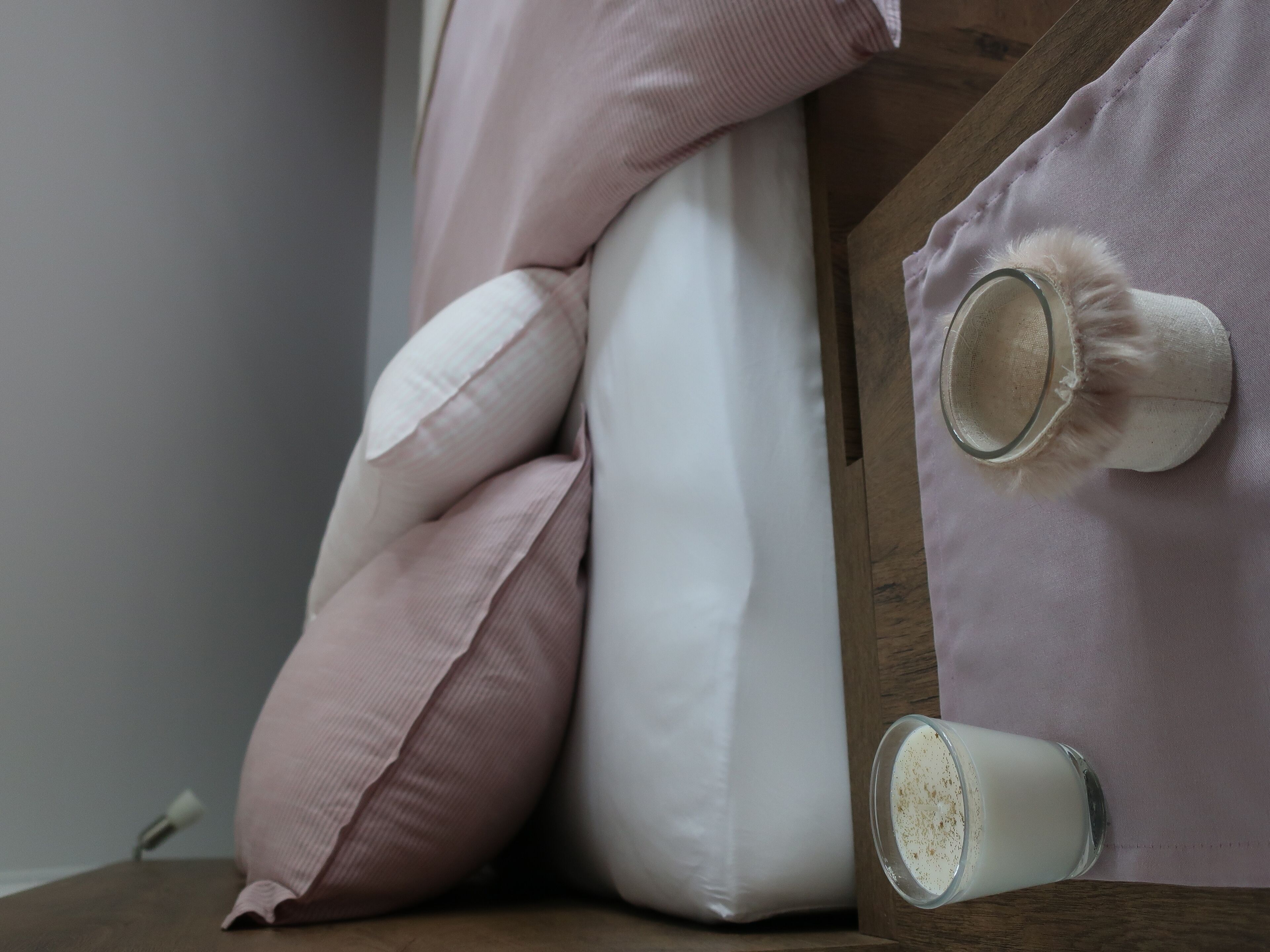 A bed with a wooden headboard, a white pillow, a pink pillow, and a glass of milk on the side.