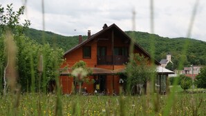 A two-story wooden house with a balcony, surrounded by a field of yellow flowers and green trees. - Apartment Jan, Pakaljski odvojak 4, 53220 Otočac, Licko-Senjska county, Croatia (Otočac)