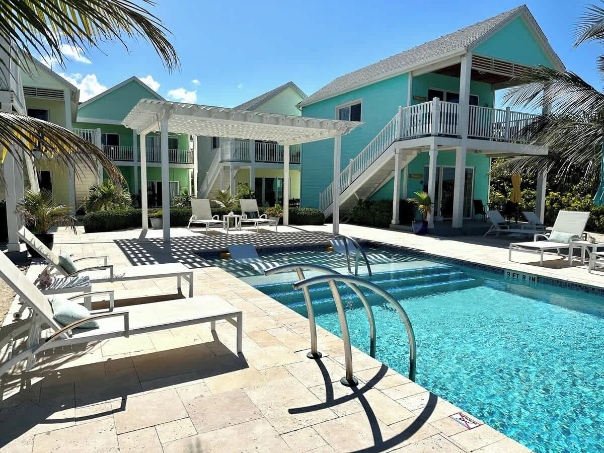 A pool area with lounge chairs and a staircase leading to a building with balconies.
