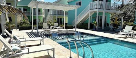 A pool area with lounge chairs and a staircase leading to a building with balconies.