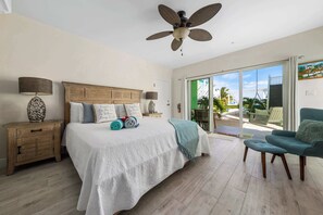 Une chambre dotée d’un grand lit, d’un ventilateur de plafond, d’une table de chevet, d’une chaise et offrant une vue sur l’extérieur.