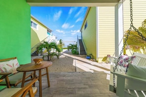 Un espace extérieur abrité comprenant une table et un banc en bois, une balançoire et une vue sur un bâtiment jaune avec un escalier menant à une passerelle couverte.