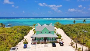 Une propriété située en bord de mer, avec une maison aux murs verdoyants, une allée en sable et une vue dégagée sur l’océan.