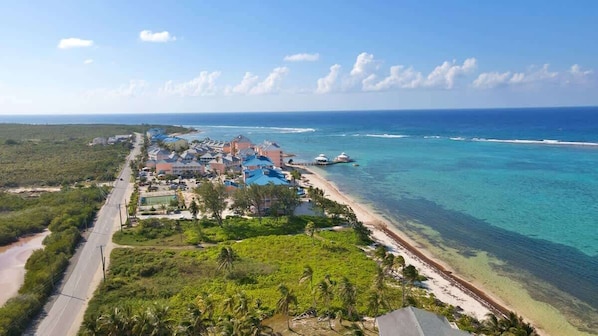 An aerial view of a coastal resort with a beachfront, a road, and a cluster of buildings with blue roofs.