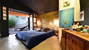 Un dormitorio con una cama grande, un aparador de madera y una estantería. Se ve un ventanal con vistas al exterior.