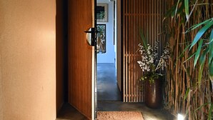 Un pasillo con una puerta de madera, una planta de bambú y un felpudo.