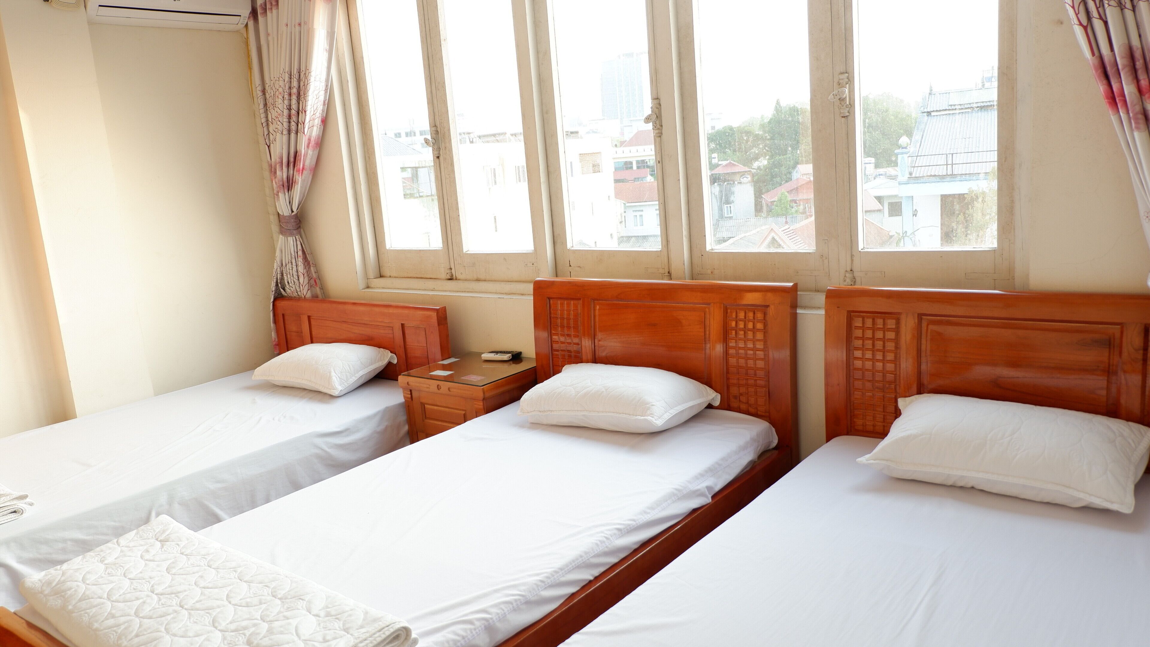 Habitación de hotel con dos camas individuales, cabeceros de madera, ropa de cama blanca, una mesita de noche con lámpara y una ventana con cortinas.