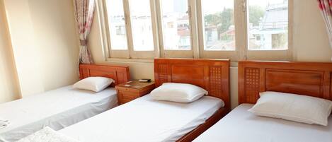 Habitación de hotel con dos camas individuales, cabeceros de madera, ropa de cama blanca, una mesita de noche con lámpara y una ventana con cortinas.