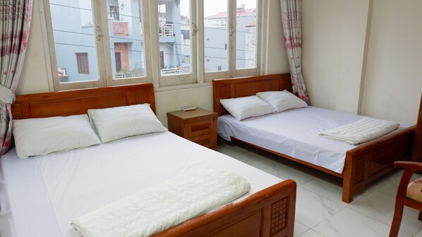 A bedroom with two single beds, wooden headboards, white bedding, a small bedside table, and a window with curtains.