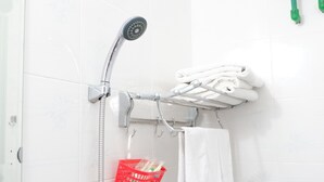 Une douche équipée d’un pommeau de douche à main, un porte-serviettes avec des serviettes et un panier rouge contenant des articles de toilette.