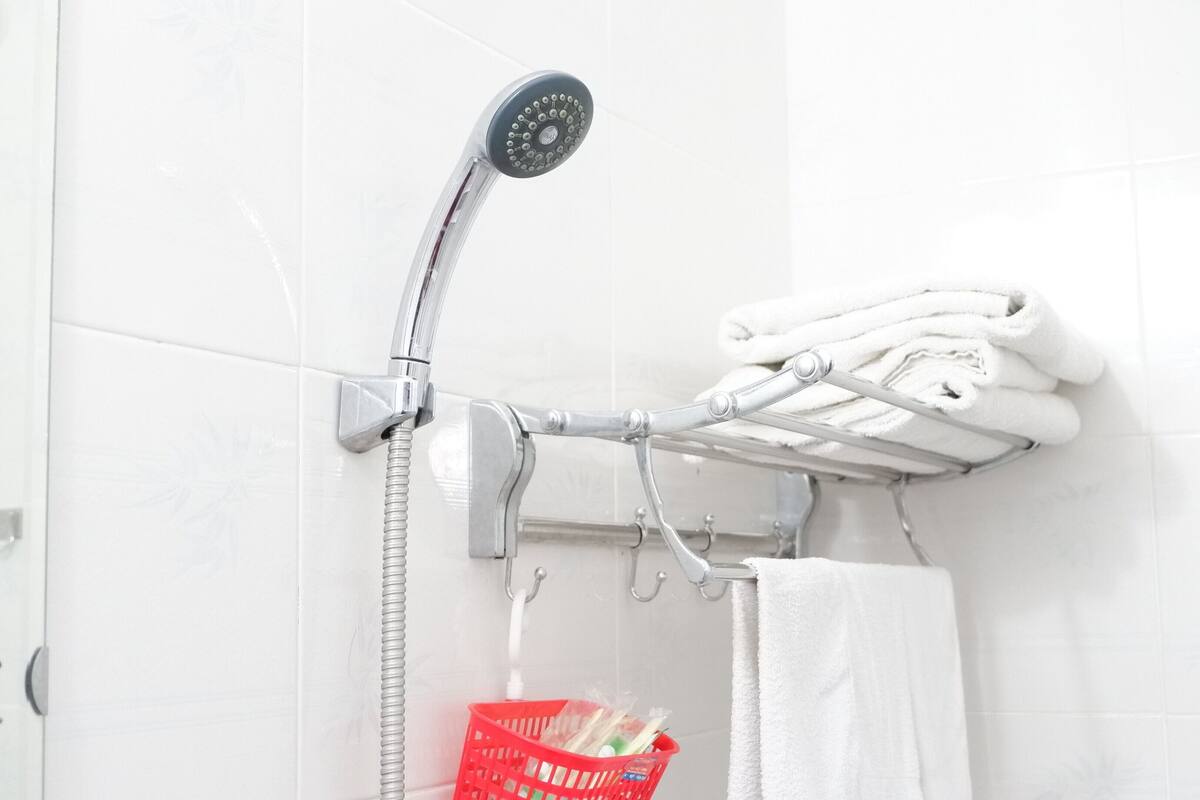 Suihkussa on käsisuihkupää, pyyhetelineessä on pyyhkeitä ja punaisessa korissa on hygieniatuotteita.