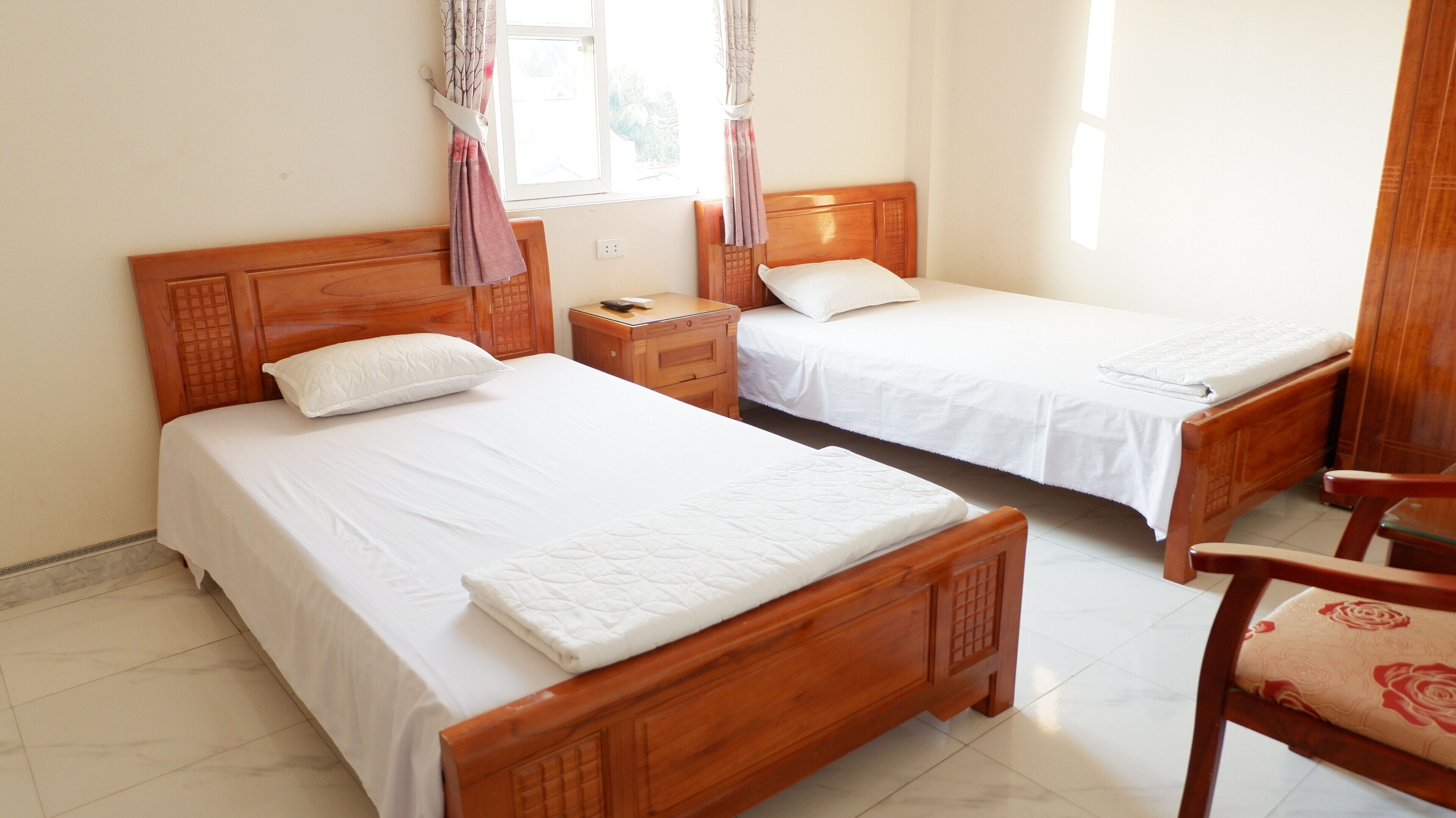 A hotel room with two wooden beds, a nightstand, a chair, and a window with curtains.