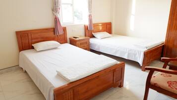 A hotel room with two wooden beds, a nightstand, a chair, and a window with curtains.