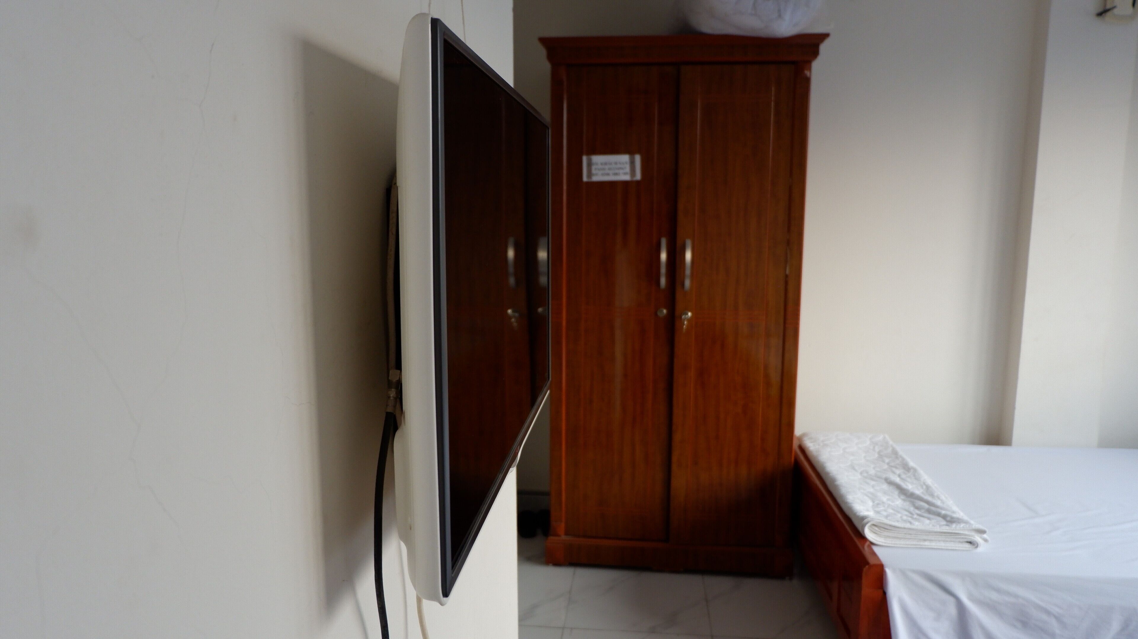Quarto com guarda-roupa de madeira, cama com colcha branca e televisão de tela plana na parede.
