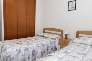 Ein Schlafzimmer mit zwei Einzelbetten, einem Holzschrank, einem Nachttisch mit Lampe und einem gerahmten Bild an der Wand.