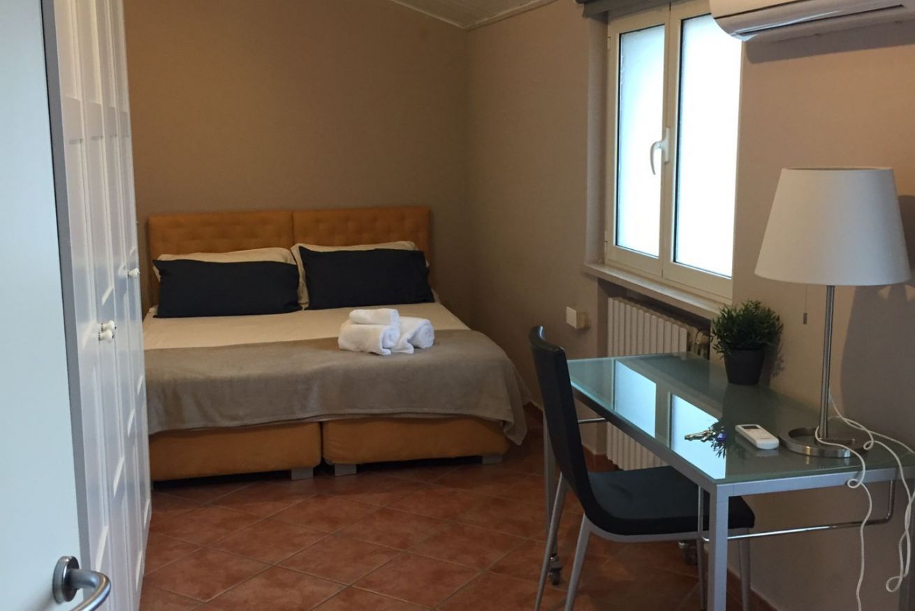 A hotel room with a bed, a desk, a chair, a lamp, and a window.