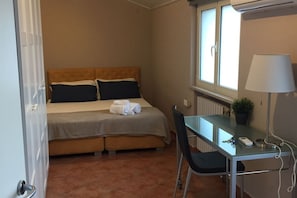A hotel room with a bed, a desk, a chair, a lamp, and a window.
