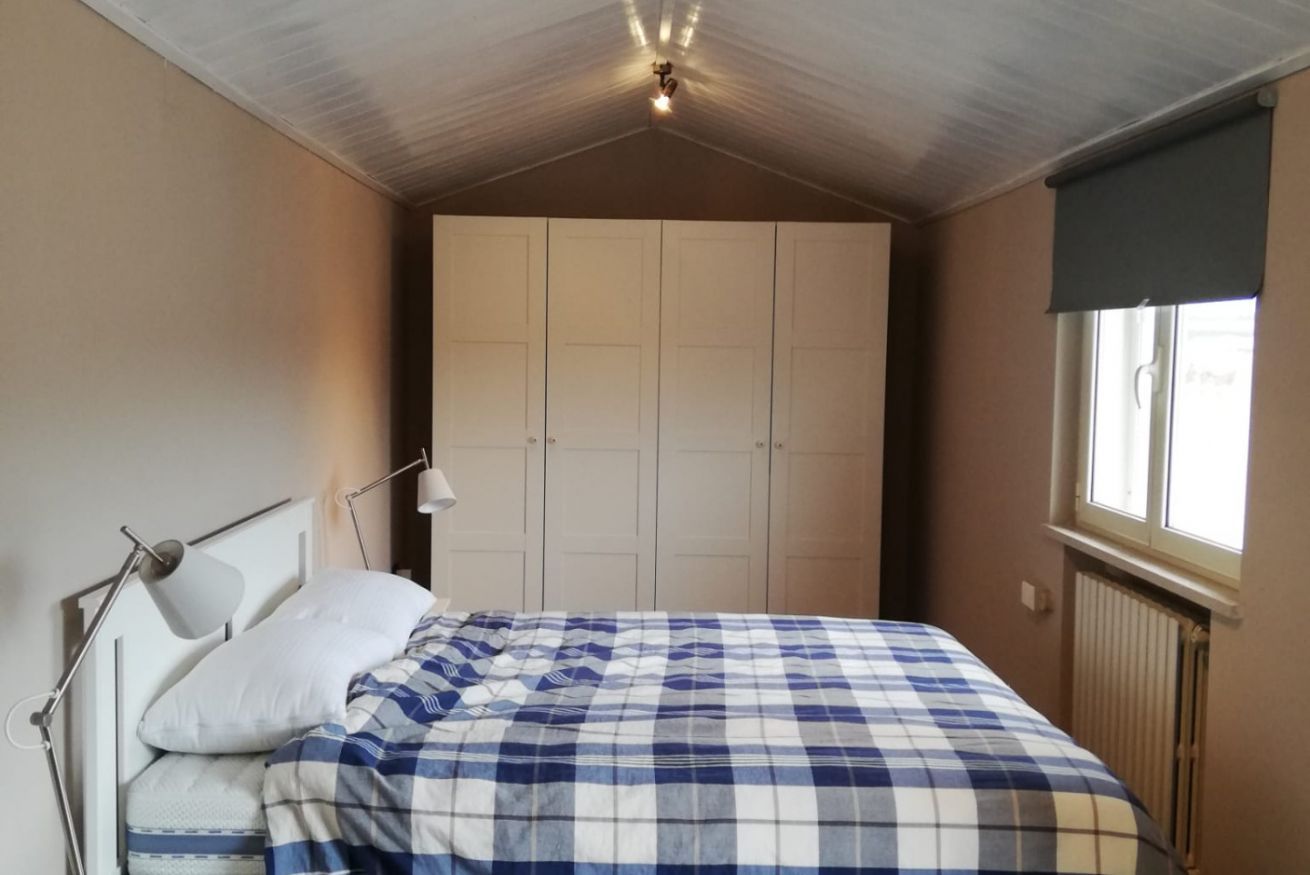 A bedroom with a bed, a bedside lamp, a wardrobe, and a window with a blind.