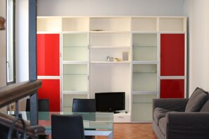 A modern living room with a glass coffee table, a flat-screen TV, a grey sofa, and a red and white shelving unit. - full-equipped flat in the city center of Pescara (Pescara)