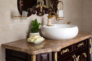 Un baño con un lavamanos grande de color blanco, grifos dorados y encimera de mármol.