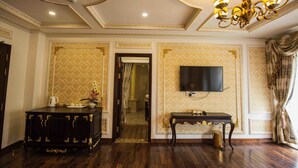 A room with a dark wooden floor, a black ornate cabinet, a small table with a lamp, and a television mounted on the wall. - Sepia Hotel DaLat (Xuan Huong - Da Lat)