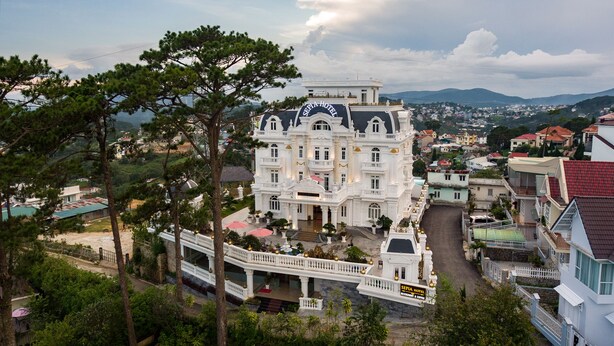 A large, white, multi-story hotel with a grand entrance and a prominent sign. - Sepia Hotel DaLat (Xuan Huong - Da Lat)