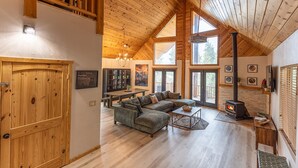 Un salon spacieux avec un plafond en bois, un grand canapé, une cheminée et un coin repas.
