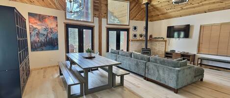 A spacious living area with a wooden ceiling, large windows, a fireplace, and a sofa.
