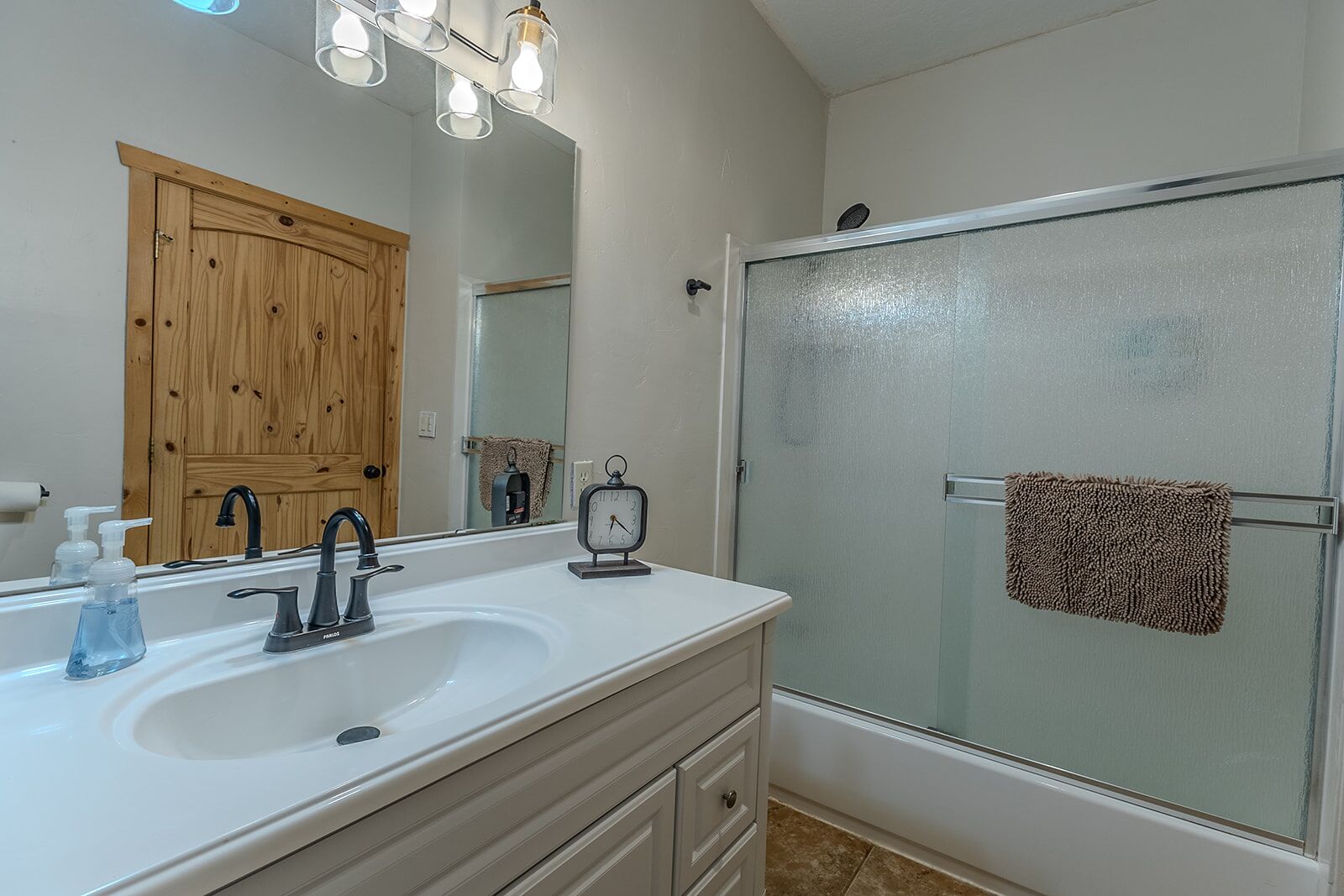 Une salle de bain avec un meuble-lavabo en bois, un évier, un miroir, une douche avec une porte en verre et un porte-serviettes.