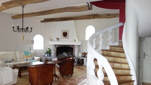 A spacious living room with a fireplace, a white staircase, and a chandelier. - Charming Provencal farmhouse, nice and well located, with pool (Cagnes-Sur-Mer)