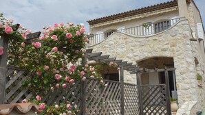 A stone building with a balcony and a wooden fence with pink roses. - Charming Provencal farmhouse, nice and well located, with pool (Cagnes-Sur-Mer)