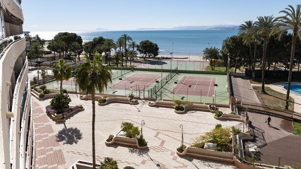 Un court de tennis avec une piscine et des palmiers, offrant une vue sur la mer.