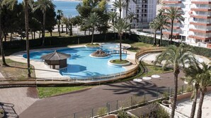 Un complexe hôtelier doté d’une piscine centrale, de palmiers et offrant une vue sur la mer et les montagnes.