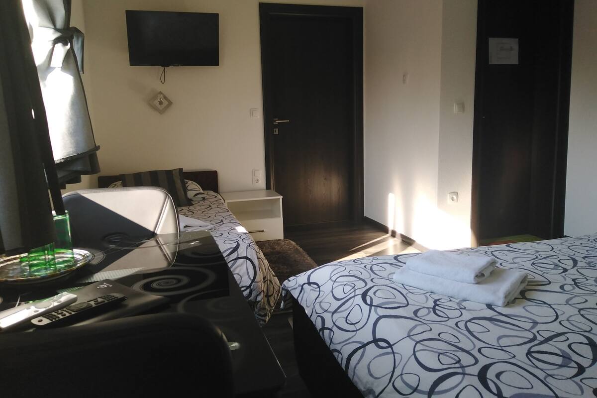 A hotel room with a bed, a desk with a computer, a TV mounted on the wall, and a door.