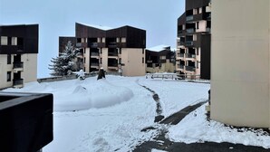 En snedækket gårdsplads med moderne lejlighedskomplekser, et sneklædt træ og en klar himmel.